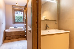 A bedroom with a wooden bed, a window, and a bathroom with a sink and mirror. - Apt Elegant With Balcony 5p/2br - Megeve Center (Megeve)