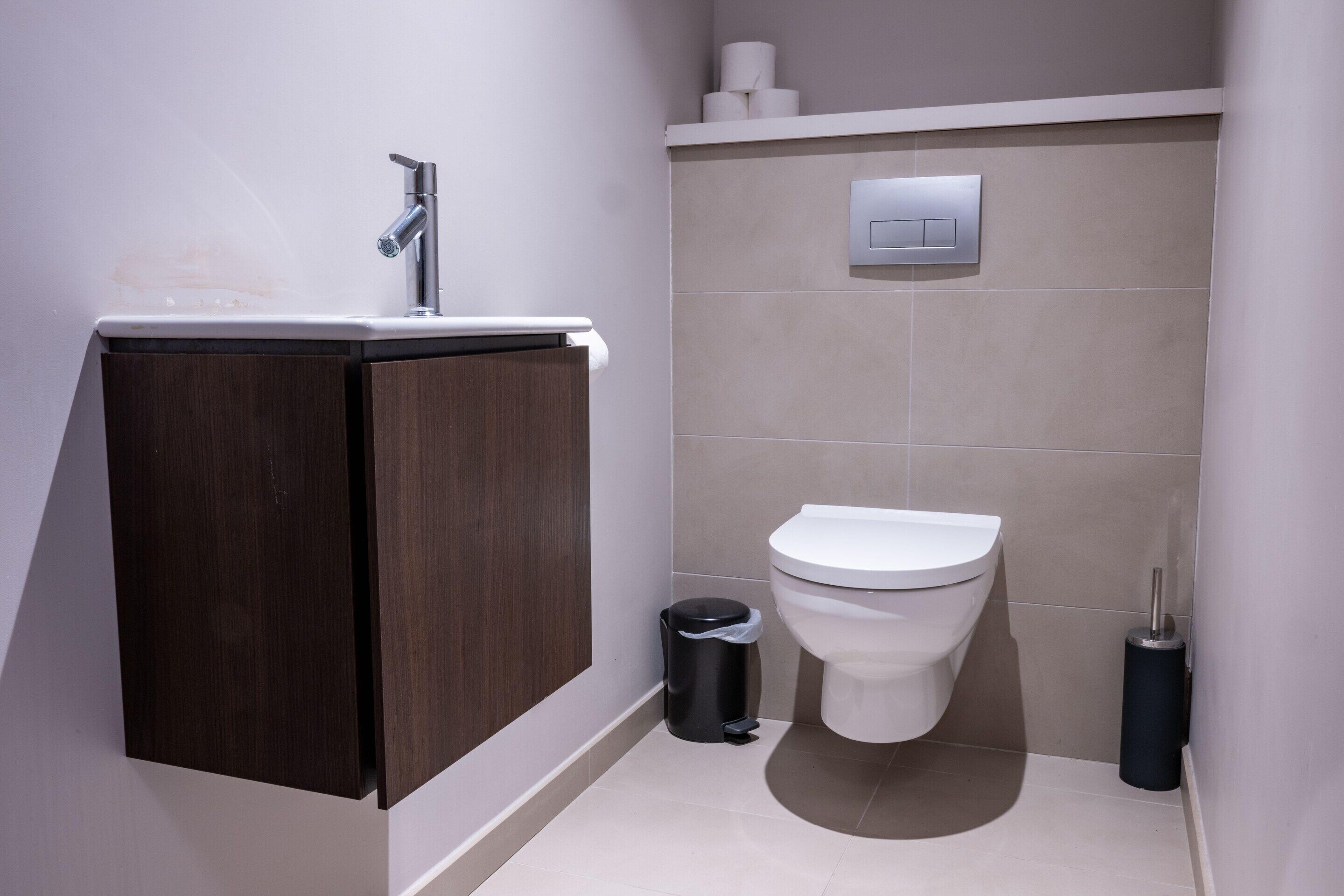 Een moderne badkamer met een donker houten kastje, een witte wastafel, een toilet en een prullenbak.