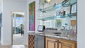 A kitchen with granite countertops, a stainless steel refrigerator, wooden cabinets, and a glass display case with kitchenware. - The Moorings 101 (Orange Beach)