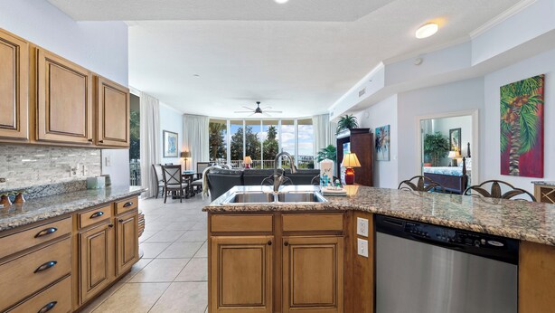 A spacious kitchen with granite countertops, wooden cabinets, and a dishwasher. - The Moorings 101 (Orange Beach)