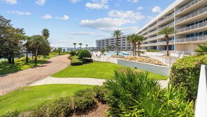 A hotel with a pool, palm trees, and a well-maintained lawn. - The Moorings 101 (Orange Beach)