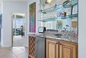 A kitchen with granite countertops, a stainless steel refrigerator, wooden cabinets, and a glass display case with kitchenware. - The Moorings 101 (Orange Beach)