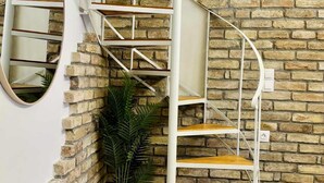 A spiral staircase with white railings and wooden steps, against a brick wall with a potted plant.