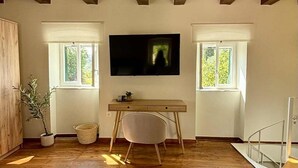 A spacious room with wooden floors, a desk, a chair, and a television mounted on the wall.