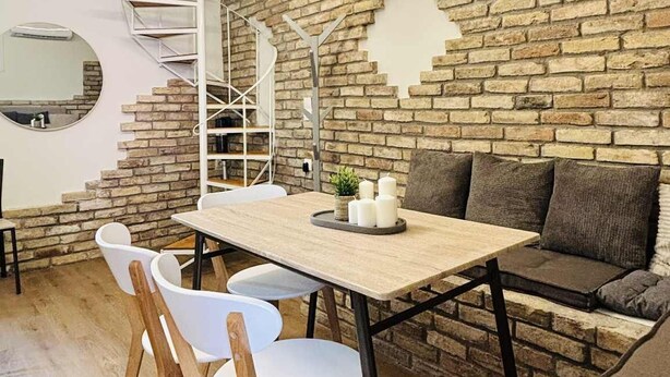 A dining area with a brick wall, a spiral staircase, and a round mirror.