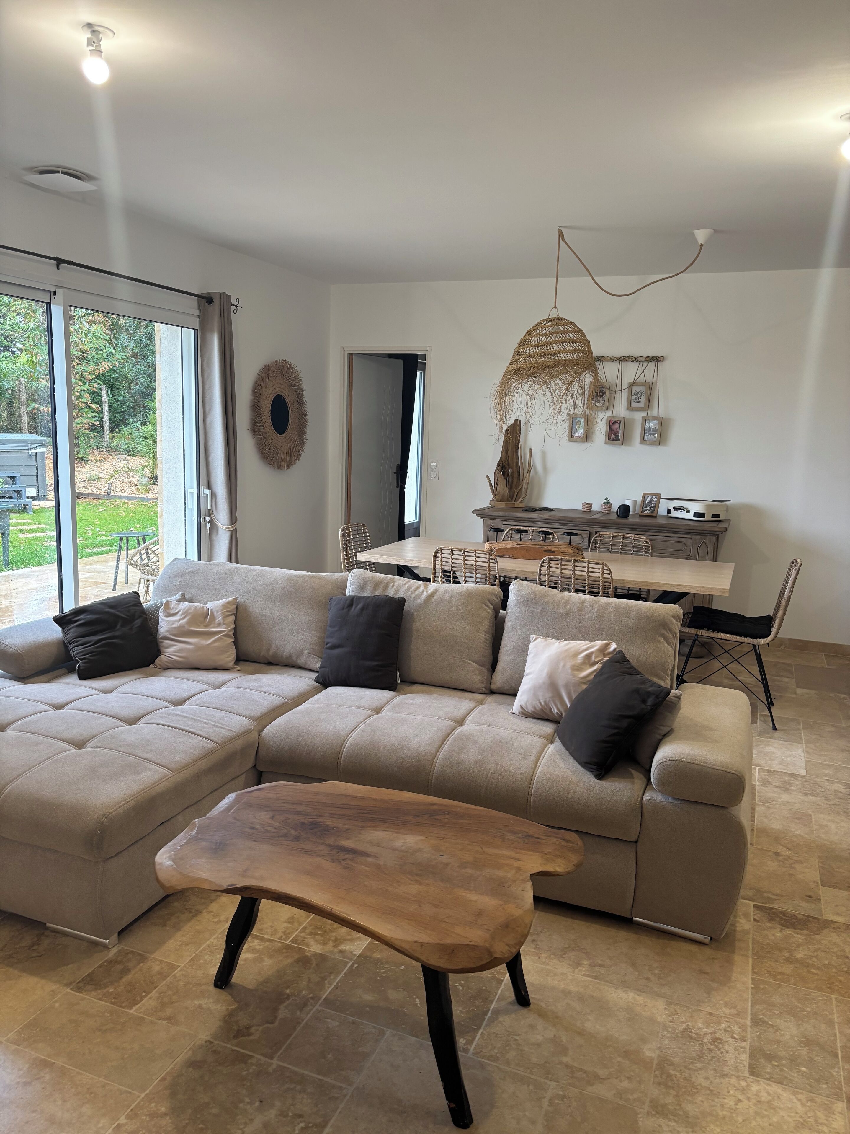 A modern living room with a sectional sofa, a wooden coffee table, and a dining area with a hanging light fixture.