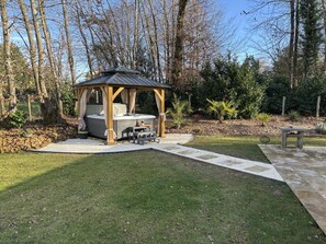 Un bain à remous installé sous une pergola en bois, dans un jardin aménagé avec un chemin de pierre et un espace détente.