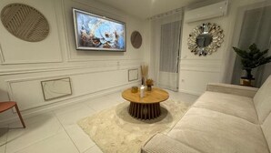 Ein modernes Wohnzimmer mit einem runden Holztisch, beigen Sofas, einem Flachbildfernseher, Wanddekoration und einem Topf mit Pflanze.