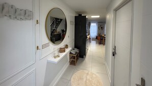 Ein Flur mit einer weißen Tür, einem Spiegel, einem Regal mit Dekoration, einer Treppe und einem Essbereich mit Tisch und Stühlen.