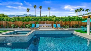 A swimming pool with lounge chairs, a fire pit, and a wooden fence with greenery. - The Spacious Open Palms (Palm Springs)