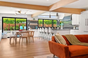 Uma cozinha moderna com armários brancos, uma área de jantar com cadeiras de madeira e grandes janelas com vista para o verde.