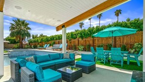 A covered outdoor area with a pool, wicker furniture, and a wooden fence. - The Spacious Open Palms (Palm Springs)