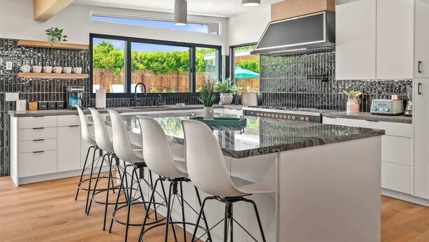 A modern kitchen with a central island, bar stools, and a large window offering a view of the outdoors. - The Spacious Open Palms (Palm Springs)
