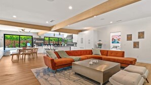 A modern living room with a sectional sofa, a coffee table, and a dining area with a table and chairs. - The Spacious Open Palms (Palm Springs)