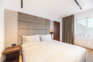 A hotel room with a large bed, a wooden nightstand, a wall-mounted headboard, a bedside lamp, and a window with curtains. - Eskaperdo Resort (Zetea)