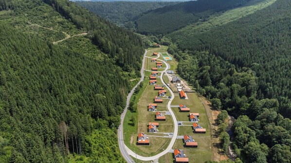 An aerial view of a residential area with houses arranged in a linear pattern along a road, surrounded by dense forest. - Eskaperdo Resort (Zetea)