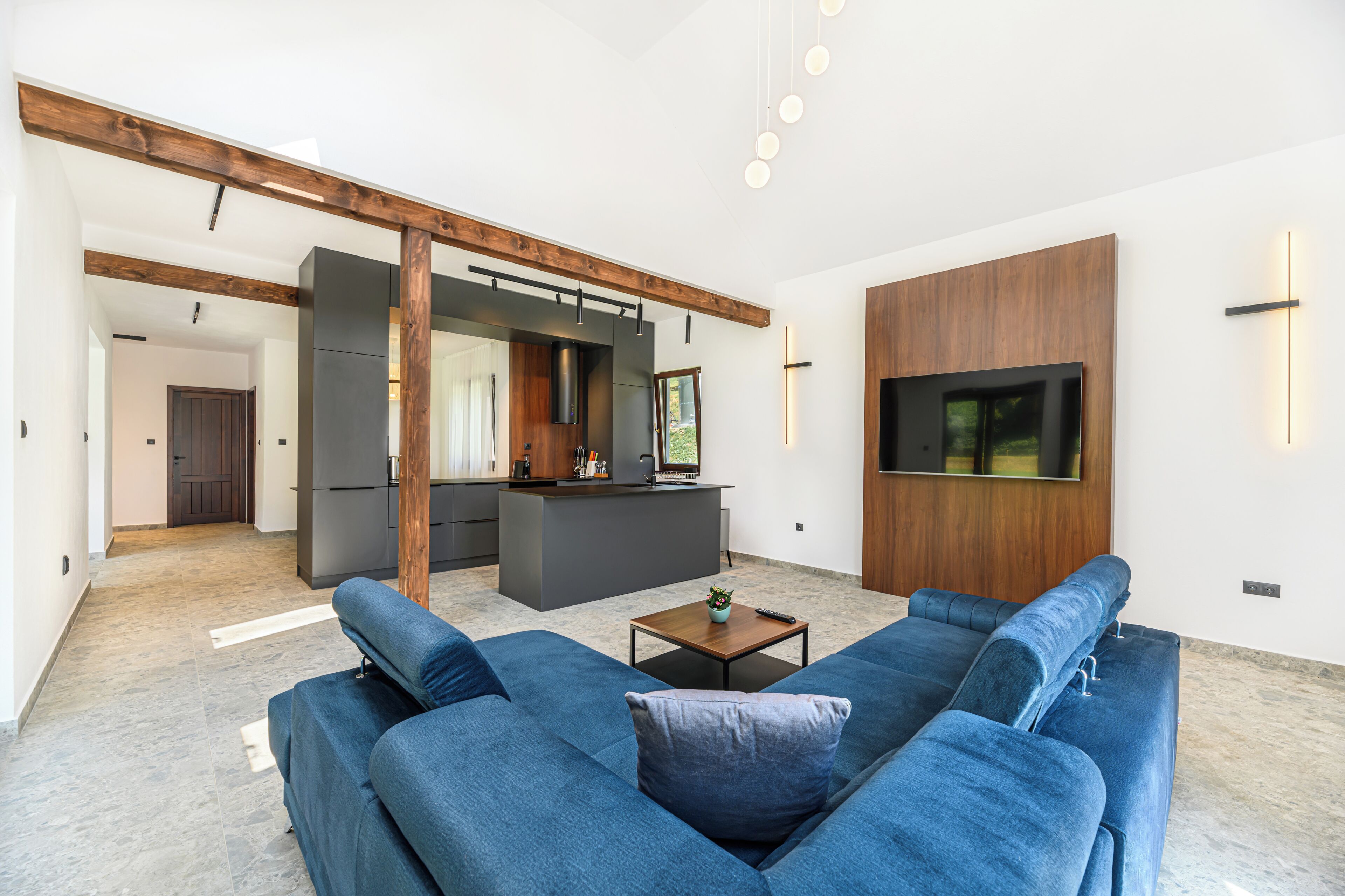 A modern living room with a blue sofa set, a wooden coffee table, and a kitchen area in the background.