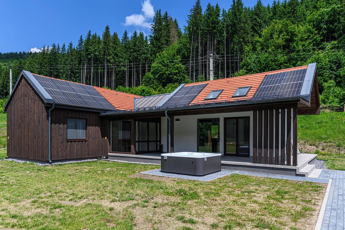 Una casa moderna con techo inclinado, paneles solares y un jacuzzi en el jardín.