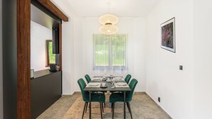 Ein Essbereich mit einem für sechs Personen gedeckten Tisch, grünen Polsterstühlen, einer Pendelleuchte und einem gerahmten Bild an der Wand.