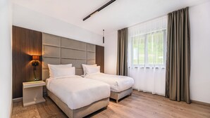 Ein modernes Schlafzimmer mit zwei Betten, einem Nachttisch, einer Wandleuchte und einem Fenster mit Vorhängen.