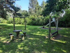 A playground with a swing set and a slide, surrounded by grass and trees. - 5 Person Holiday Home in Eskebjerg (Eskebjerg)