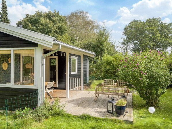 A wooden deck with a covered seating area, a small garden with a bird feeder, and a house with a porch.