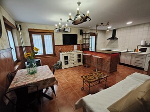 Cocina compacta con comedor, un sofá y un televisor montado en la pared.