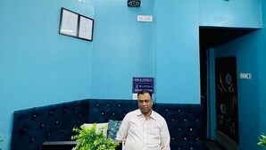 A reception area with a blue wall, a sign indicating 'NON ALCOHOLIC', and a reception desk with a plant and brochures. - RR GUEST HOUSE (Kolkata)