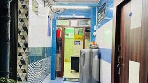A narrow hallway with a blue tiled floor, a metal door on the right, and a refrigerator in the center. - RR GUEST HOUSE (Kolkata)
