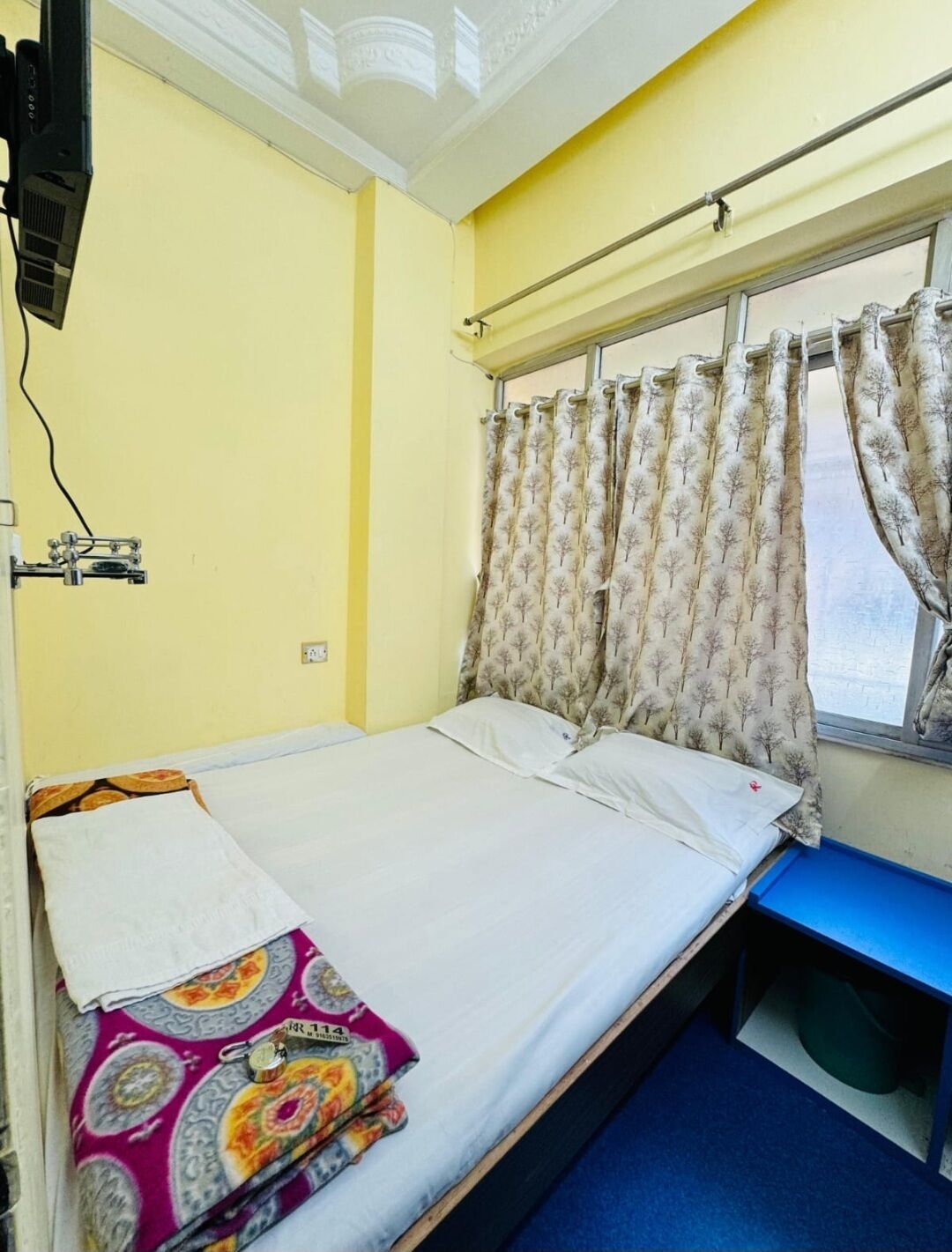 Una cama individual con sábana blanca, manta estampada y ventana con cortinas.