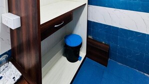A small, compact room with a wooden wardrobe, a white shelf, a blue tiled wall, and a blue floor mat. - RR GUEST HOUSE (Kolkata)