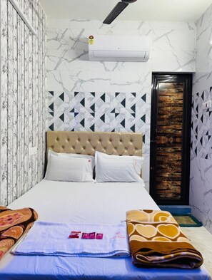A bedroom with a tufted headboard, a bed with white linens, a blue towel, and a brown patterned blanket. - RR GUEST HOUSE (Kolkata)
