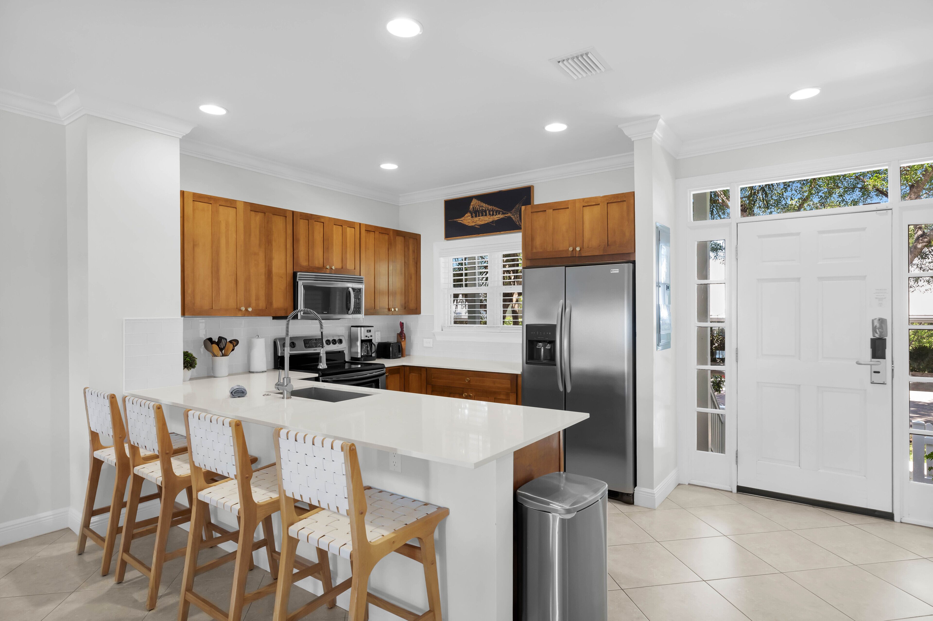 A modern kitchen with white cabinetry, a stainless steel refrigerator, and a central island with bar stools.