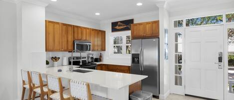 A modern kitchen with white cabinetry, a stainless steel refrigerator, and a central island with bar stools.