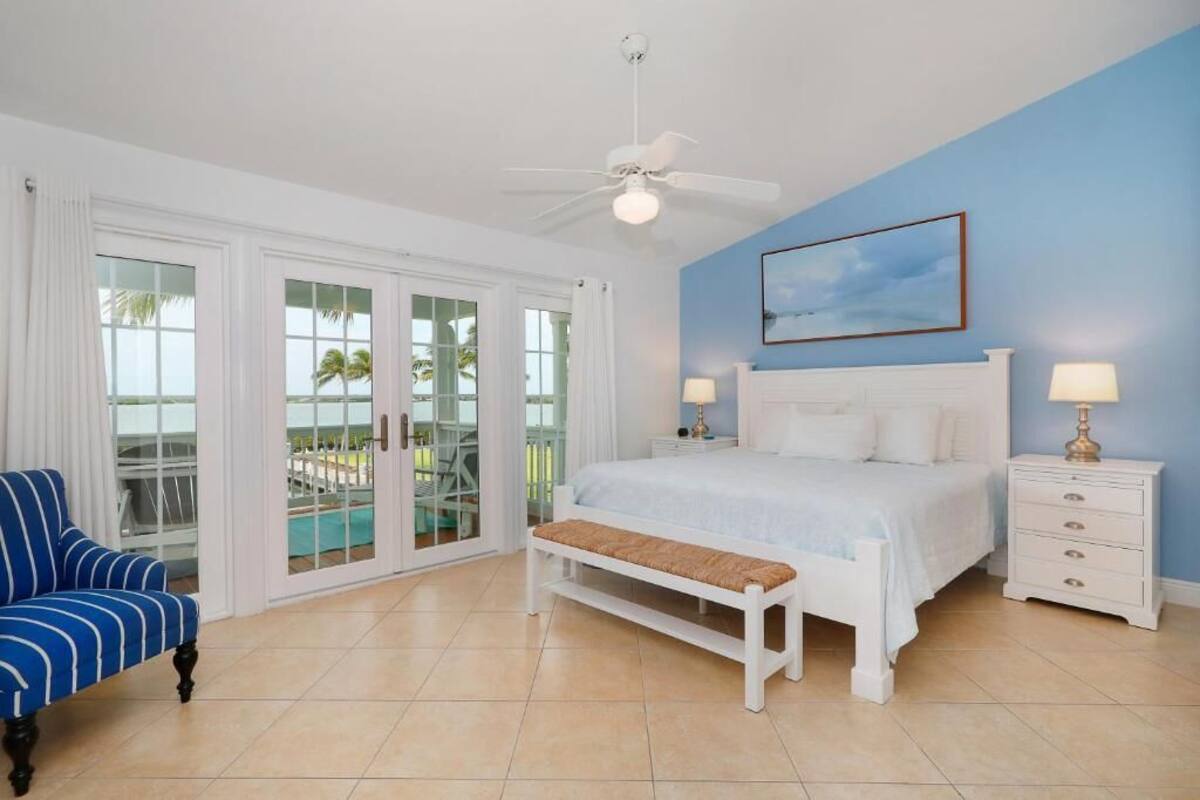 A bedroom with a bed, a bench, a nightstand, a chair, and a ceiling fan.