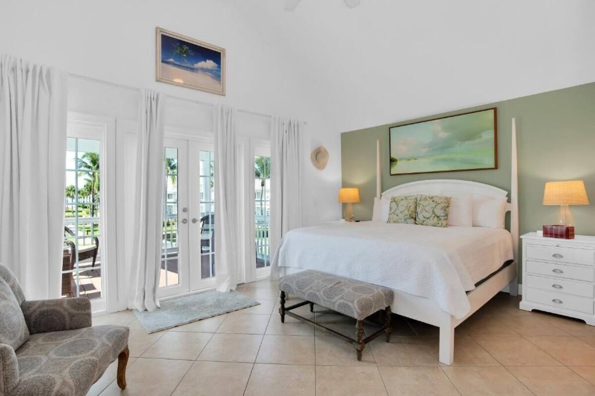 A bedroom with a bed, bedside tables, a bench, a chair, and a view of the outdoors.