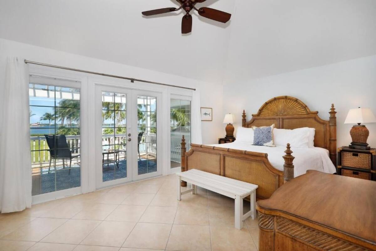A bedroom with a bed, a bench, a ceiling fan, and a view of the outdoors through large sliding glass doors.