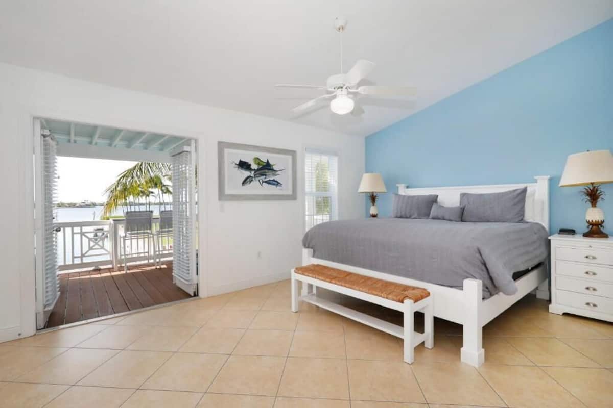 A bedroom with a bed, bedside tables, a ceiling fan, and a view of the outdoors.
