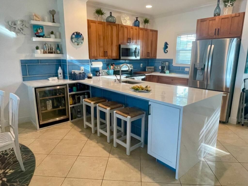 Una cocina moderna con una isla central, armarios de madera, un refrigerador de acero inoxidable y un salpicadero azul.