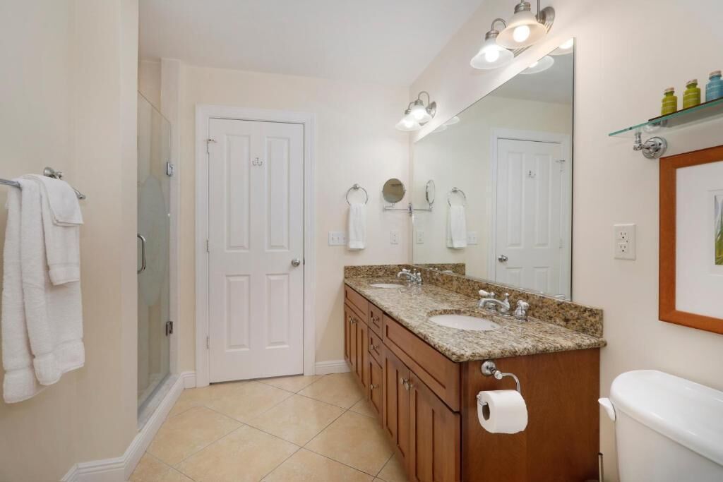 A bathroom with a double sink vanity, a large mirror, a shower, and a toilet.