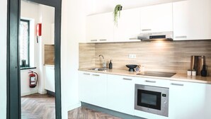 Una cocina moderna con armarios blancos, encimera de madera, pileta de acero inoxidable, microondas y una planta colgante.