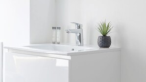 Un tocador blanco con un lavabo, un espejo y una planta pequeña en la parte superior.