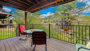 A wooden deck with a table and chairs, a red chair, and a view of trees and hills.