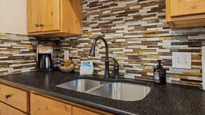 A kitchen with a granite countertop, stainless steel sink, wooden cabinets, and a mosaic tile backsplash.