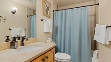 A bathroom with a marble sink, a toilet, a shower curtain, and a mirror.