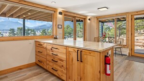 A kitchen with wooden cabinets, a marble countertop, and large windows offering a mountain view.