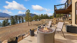 A patio with a fire pit, outdoor furniture, and a view of a lake and mountains.