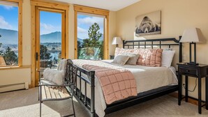 A bedroom with a bed, a chair, a nightstand, and a window with a view of mountains and trees.