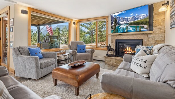 A cozy living room with a fireplace, comfortable seating, and a large TV screen displaying a scenic view.