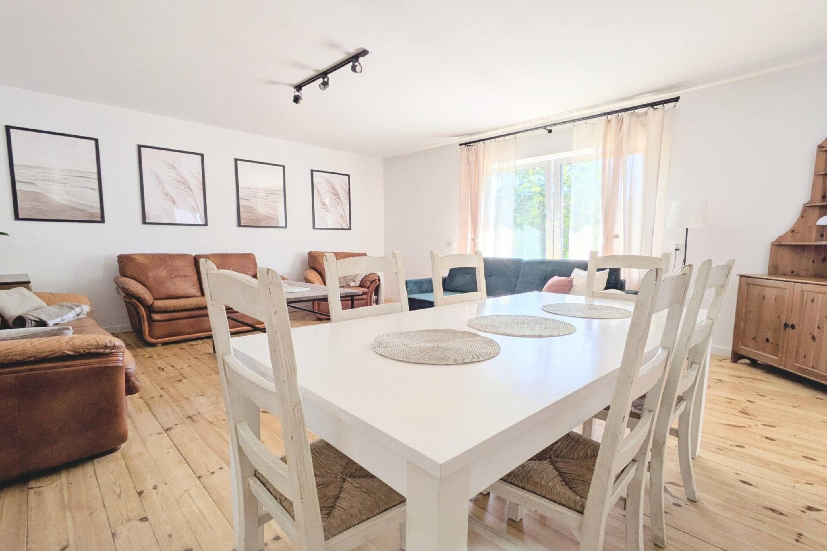 A dining area with a white table and chairs, a brown sofa, and a wooden cabinet.